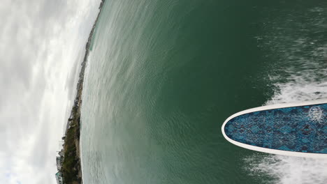 Vertical-shot-of-a-man-surfing-a-wave-on-a-longboard-in-Riverton,-New-Zealand
