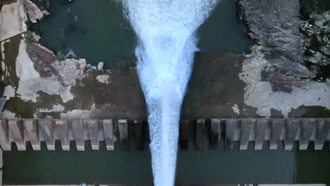 Dam-pouring-water-to-almost-empty-reservoir-due-to-drought,-aerial-top-down-view