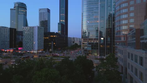 Aerial-perspective-of-Warsaw,-unveiling-the-iconic-Rondo-ONZ-in-the-vibrant-city-center,-with-the-evening-traffic-and-captivating-reflections