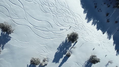 Aerial-View-of-Snowboarder-Skiing-Downhill-on-Sunny-Winter-Day,-High-Angle-Drone-Shot