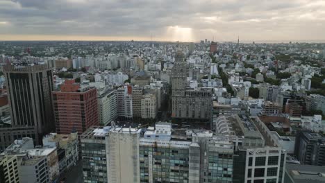 Montevideo-reverse-aerial-view-over-downtown-Uruguay-city-blocks-with-sunrays-cloudscape-across-the-skyline