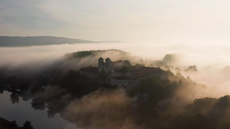 Aerial-drone-view-of-Benedictine-Abbey-over-Vistula-river-in-Tyniec-in-the-morning-fog,-Krakow,-Poland