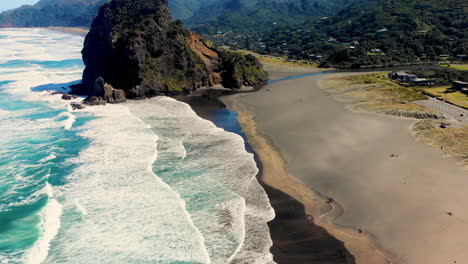 Fly-over-Piha-Beach-to-rock-formation,-popular-tourist-and-holiday-spot,-New-Zealand