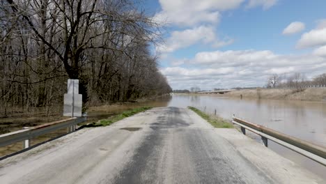 Close-up-of-flooded-rural-road-in-southern-Indiana-with-drone-video-moving-forward-and-rising-up-to-wide-shot