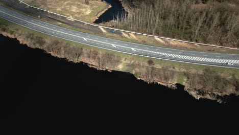 Aerial-view-of-a-two-lane-road-with-passing-cars-surrounded-by-lakes-and-spring-nature