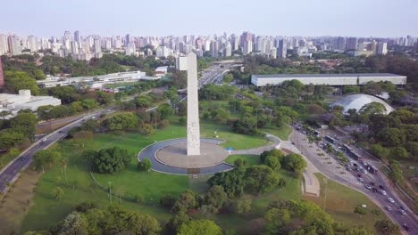 Obelisco-landmark-with-the-skyline-of-Sao-Paolo-in-Brazil--descending-aerial-shot,-sunset-summer-day