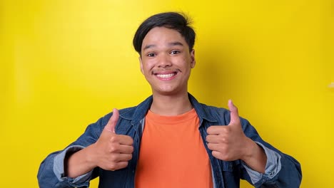 Young-man-in-casual-style-showing-thumbs-up-and-dance-isolated-on-yellow-background