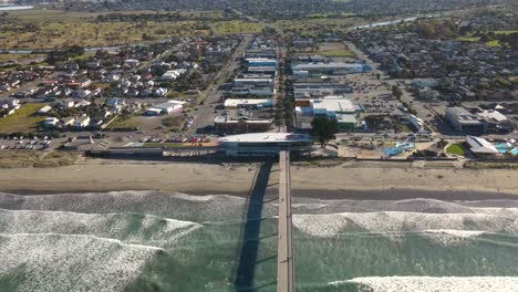 Outstanding-aerial-view-of-coastal-cityscape-of-ocean-waving-long-sandy-beach,-seaside-housing-area-and-people-walking-on-pier