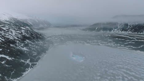 Paisaje-Islandés-Congelado-En-Temporada-De-Invierno,-Vista-Aérea-Del-Lago-Glacial,-Iceberg-Y-Colinas-Volcánicas-Cubiertas-De-Nieve