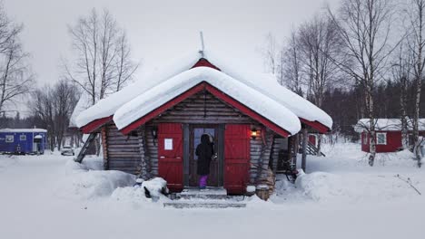 Lady-walking-into-cute-picturesque-wooden-cabin-in-nature-with-snow