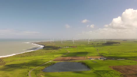 Wind-farm-in-the-middle-of-farmland-on-coastal---drone-pull-back