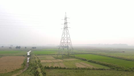 Aerial-drone-rising-by-high-tension-pylon-in-countryside-environment,-foggy-day