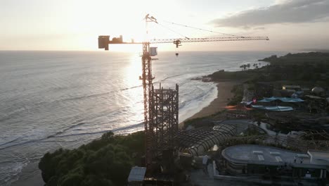 Sunset-ocean-aerial-rotates-around-tower-crane-on-construction-site