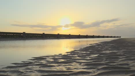Rippled-sand-and-calm-water-with-breakwater-in-slow-motion-at-sunset-at-Fleetwood,-Lancashire,-UK