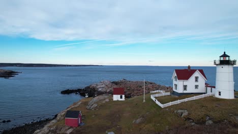 Flyover-of-lighthouse-on-a-rocky-coastal-island-with-rippling-water-and-blue-sky-above