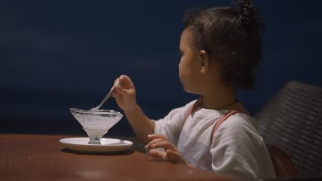 Young-girl-eating-melted-ice-cream-from-sundae-glass-with-spoon,-at-twilight