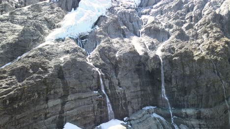Close-up-of-ice-and-snow-beeing-melted-down-to-waterfalls-falling-from-rocky-mountain-slope