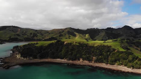 Aerial-view-of-Wilsons-Bay-surrounded-by-grassy-mountains-kereta-coromandel-new-zealand,-orbit