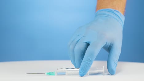 Hand-with-blue-gloves-picks-up-syringe-with-narcotic,-studio-blue-background
