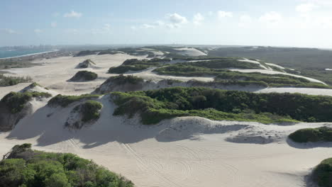 AERIAL---Beautiful-sandy-dunes-on-Genipabu-beach,-Brazil,-rising-reveal-tilt-down