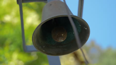 Close-Up-On-A-Small-Black-Cast-Iron-Bell-With-Trees-In-Background-in-slowmotion-in-france