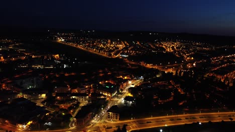 Nocturnal-aerial-view-of-a-small-city-illuminated-by-orange-city-lights,-establishing-shot