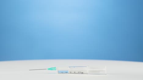 Blue-gloves-hand-places-medical-syringe-with-vaccination-down,-blue-background