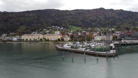 Aerial-view-of-Lake-Constance,-from-the-city-of-Bregenz,-Vorarlberg,-Austria,-Europe,-on-a-cloudy-day-breathing-autumn-tranquility,-with-the-port-and-boats-and-the-hills-in-the-background