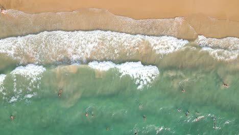 Overhead-drone-flight-over-beautiful-beach-with-turquoise-waters-and-people-swimming