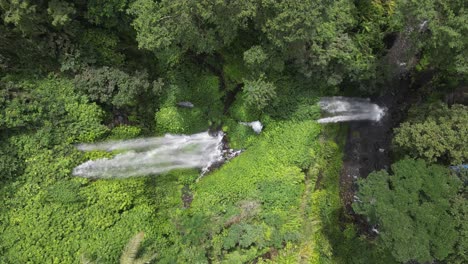 Aerial-tilts-down-dramatic-jungle-waterfall-on-mountain-slope,-Lombok