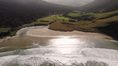 Short-beautiful-beach-aerial-shot-green-saddle-reveal-in-The-Catlins,-East-Coast,-South-Island,-New-Zealand,-nice-surfing-spot,-in-sunny-day
