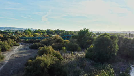 Aerial-forward-to-remote-green-railway-bridge-over-a-river-in-the-Spanish-desert
