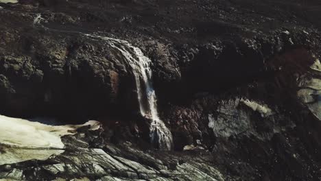 Luftpanorama-Eines-Gletscherflusses,-Der-An-Einem-Sonnigen-Tag-Einen-Wasserfall-Neben-Einem-Isländischen-Gletscher-Hinunterfließt