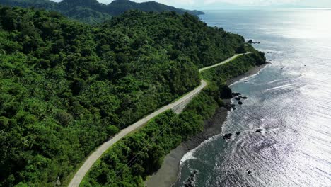 Epic-Flyover-Shot-of-Cliffside-Winding-Road-facing-Turquoise-Ocean-Waves-and-Rocky-Beach-in-tropical-island-of-Catanduanes