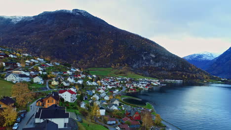 -Aerial-drone-forward-moving-shot-over-a-small-fisher-town-on-the-coast-of-a-fjord-in-Norway-surrounded-by-mountain-range-during-evening-time