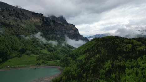 Cautivadora-Vista-Aérea-De-Los-Alpes-Suizos-Abrazados-Por-Nubes,-Frondosos-árboles-Verdes