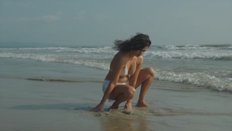 Fixed-clip-of-woman-crouching-at-shoreline-and-rinsing-her-hands-in-seawater-from-lapping-waves