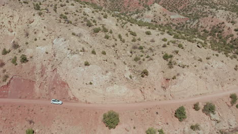 Car-drives-by-on-desert-dirt-road-on-cliffside