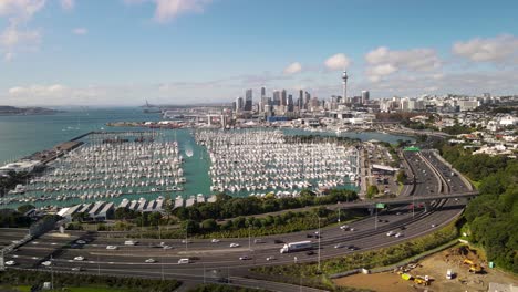 Sunny-day-in-Auckland,-aerial-sideway-of-Yacht-Club-and-CBD-cityscape-on-horizon