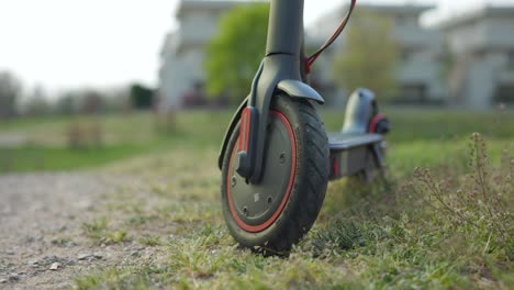 Close-up-of-electric-scooter-wheel-parked-over-grass,-circle-pan,-soft-focus