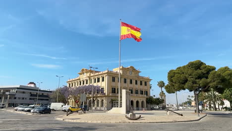Spanish-flag-waving-in-the-wind-in-slow-motion-over-Malaga-port,-Spain