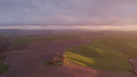 Rolling-hills-of-Tuscany-at-sunset-with-luxury-villa-farm-house,-aerial