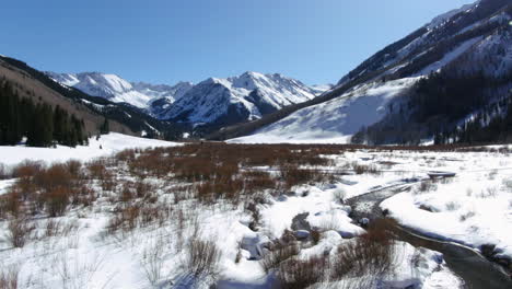 Bluebird-Sonniger-Tag-Frühling-Winter-Colorado-Wunderschöne-Aussicht-Auf-Die-Berge-Und-Friedlicher-Bach-Ashcroft-Maroon-Bells-Aspen-Colorado-Ikonische-Landschaft-Luftrückwärtsbewegung
