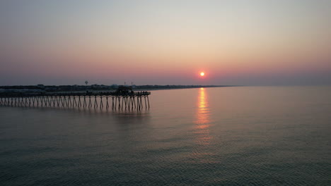 Drone-of-Bogue-Inlet-Pier-with-calm-ocean-while-the-sun-is-rising,-wide-shot