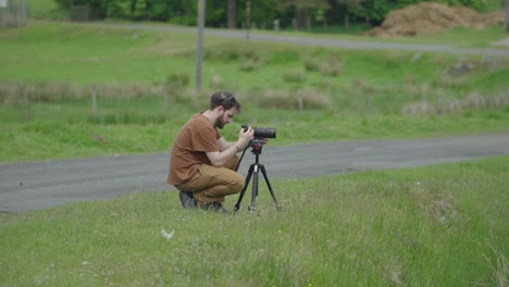 Videographer-setting-up-his-tripod-and-camera-crouching-down-on-grass