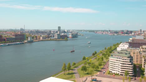 Stadtbild-Entlang-Des-IJ-Flusskanals-Mit-Booten,-Die-In-Der-Nähe-Des-Hauptbahnhofs-Von-Amsterdam-In-Den-Niederlanden-überqueren