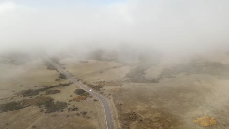 Coche-Blanco-Conduce-Por-Carretera-Rural-Hacia-La-Niebla,-Madeira,-Portugal,-Aéreo