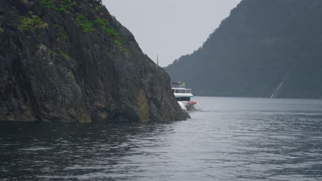 Tourist-boat-disappearing-behind-coastal-cliff-in-Milford-Sound-inlet