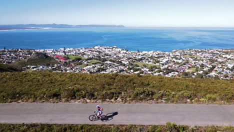 Cyclist-cycling-on-mountain-road-through-fynbos-overlooking-picturesque-Hermanus
