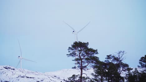 Slow-Motion-Of-Rotating-Wind-Turbine-Against-Blue-Clear-Sky-On-Snow-Mountains